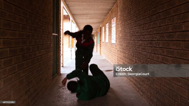 Two school kids fight in a dark passageway of their school, almost silhouette. feel